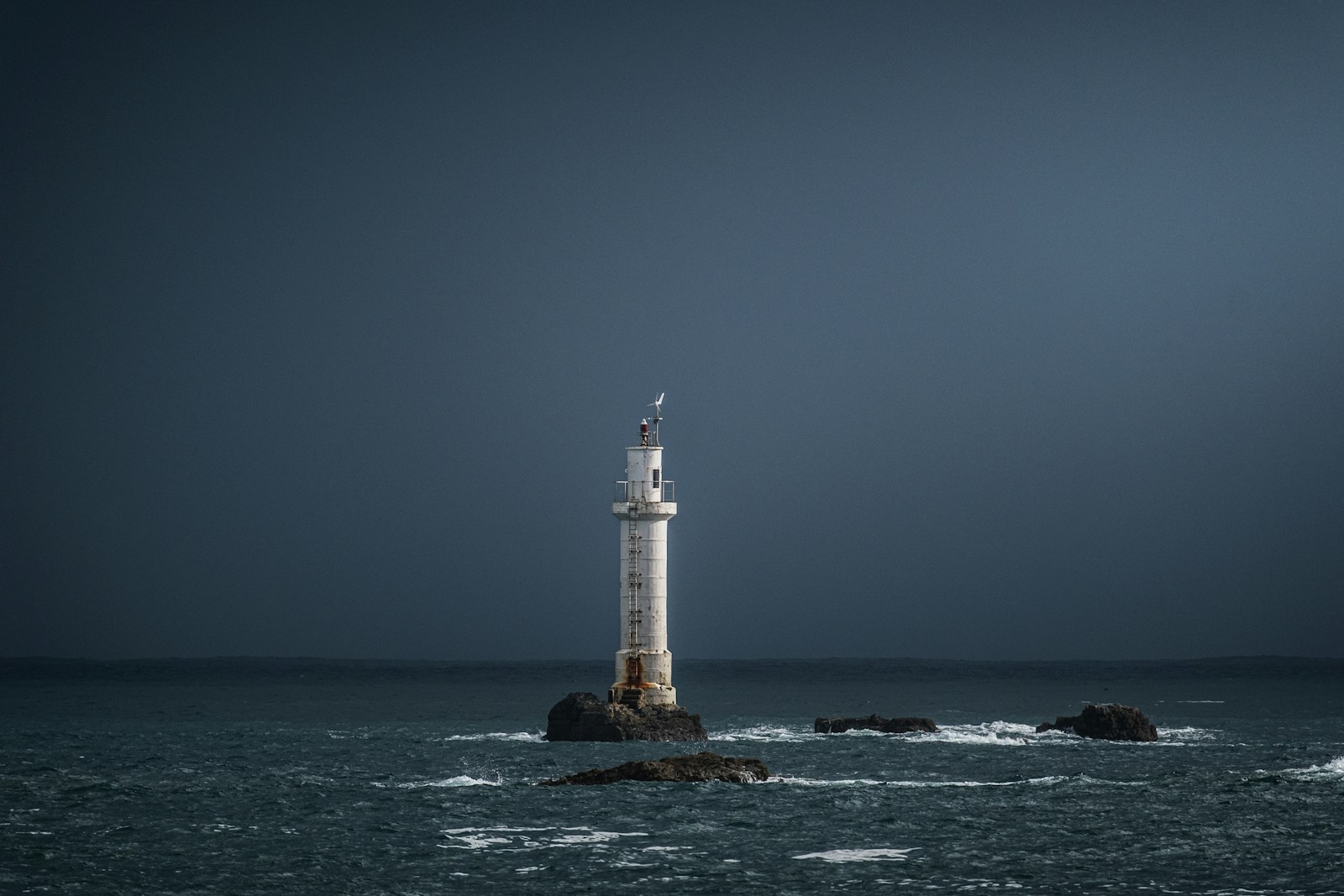 A lighthouse standing on a rock in a dark sea